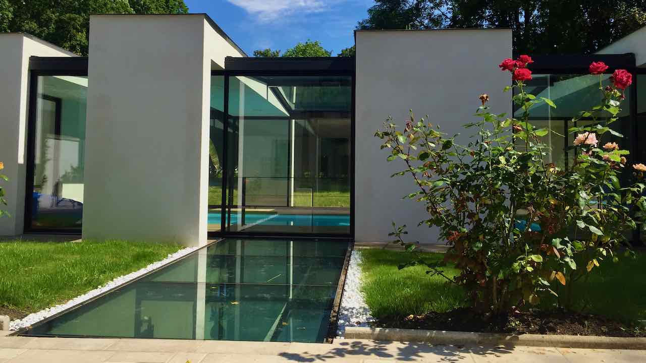 Extension d'une piscine intérieru avec baies coulissantes minimilaistes de très grandes dimensions et verrières zénithales pour un maximum de lumière naturelle