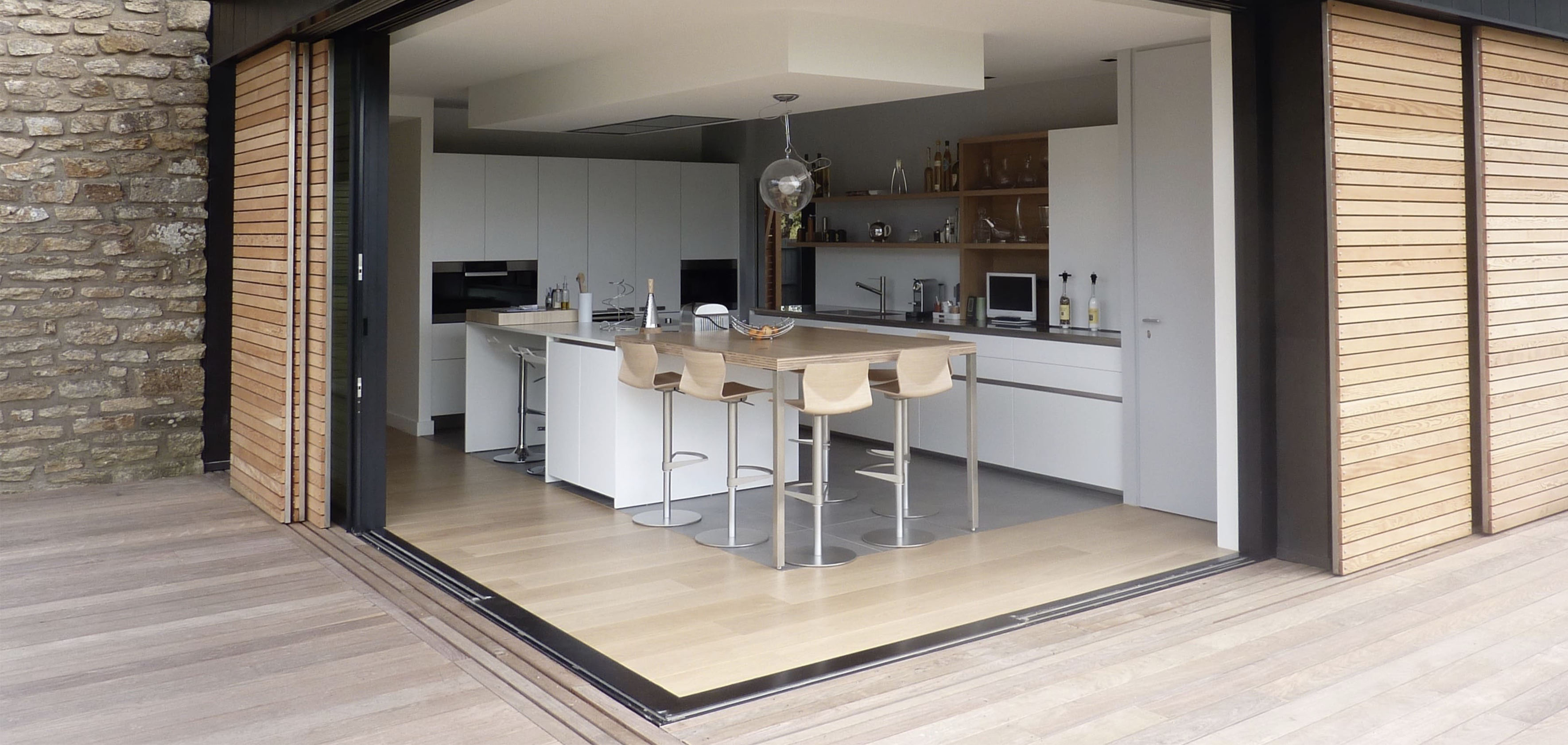 Extension d'une maison, avec cuisine totalement ouverte sur le jardin grâces à un baie ne angle à galandage